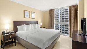 Camera d'albergo con un letto grande, due comodini con lampade, una televisione e una finestra vista su un edificio.