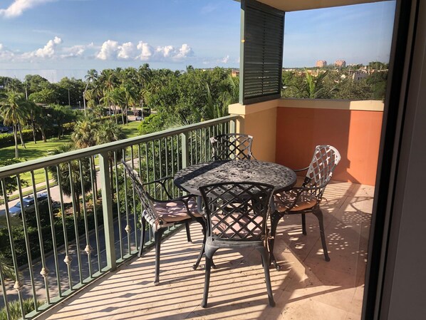 A balcony with a table and chairs, a view of a green landscape with trees and buildings in the distance.