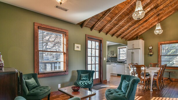 Un salón amplio con suelo de madera, sillas tapizadas en verde, una mesa de comedor y una cocina al fondo.