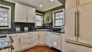 Una cocina con gabinetes blancos, encimera negra y refrigerador de acero inoxidable.