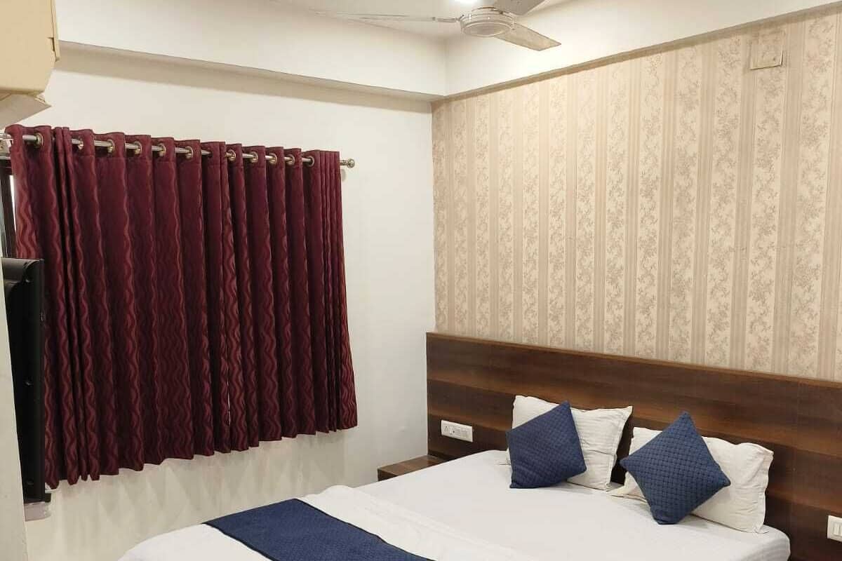 A neatly made bed with a wooden headboard, a dark red curtain, and a patterned wallpaper on the wall.