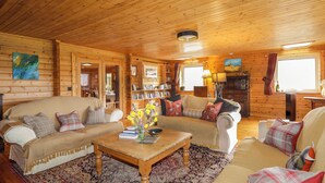 A cozy log cabin interior with two sofas, a coffee table, bookshelves, and a fireplace.