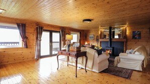 A cozy cabin interior with wooden floors, a fireplace, a sofa, and a dining table.