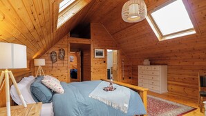 A cozy attic bedroom with a large bed, wooden walls, a skylight, and a small bathroom.