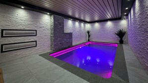 Piscina interior moderna con pared de piedra y techo de madera.