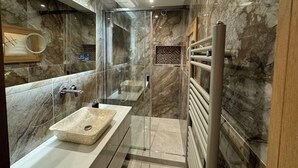 Un baño moderno con detalles de mármol, cabina de ducha de vidrio y lavamanos empotrado.