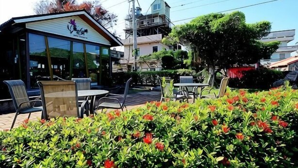 Een restaurant met terras, een glazen gevel en een tuin met rode bloemen.