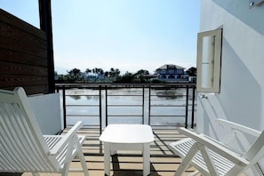 A balcony with white chairs and a table, overlooking a body of water and a distant building. - Lotus Hostel Beicheng Zhuang (Yilan)