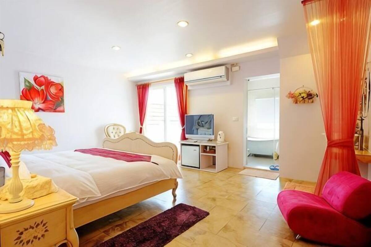 A bedroom with a bed, bedside table, TV, and a desk with a chair.