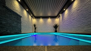 Una piscina interior moderna con iluminación azul, paredes de piedra y dos plantas en macetas.