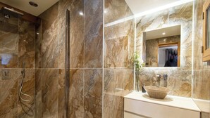 Un baño moderno con cabina de ducha de vidrio, paredes de mármol y tocador blanco con lavabo.