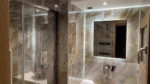 Un baño moderno con ducha envuelta en vidrio, pared de azulejos de mármol y lavamanos sobre encimera.