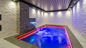 Ein Wellnessbereich mit beheiztem Pool, Steinwänden und Holzbalkendecke.