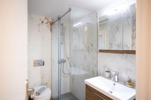 A bathroom with a glass-enclosed shower, a white sink with a mirror above it, and a toilet.