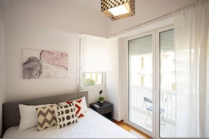 A bedroom with a bed, a nightstand, a window, and a view of the outside balcony.