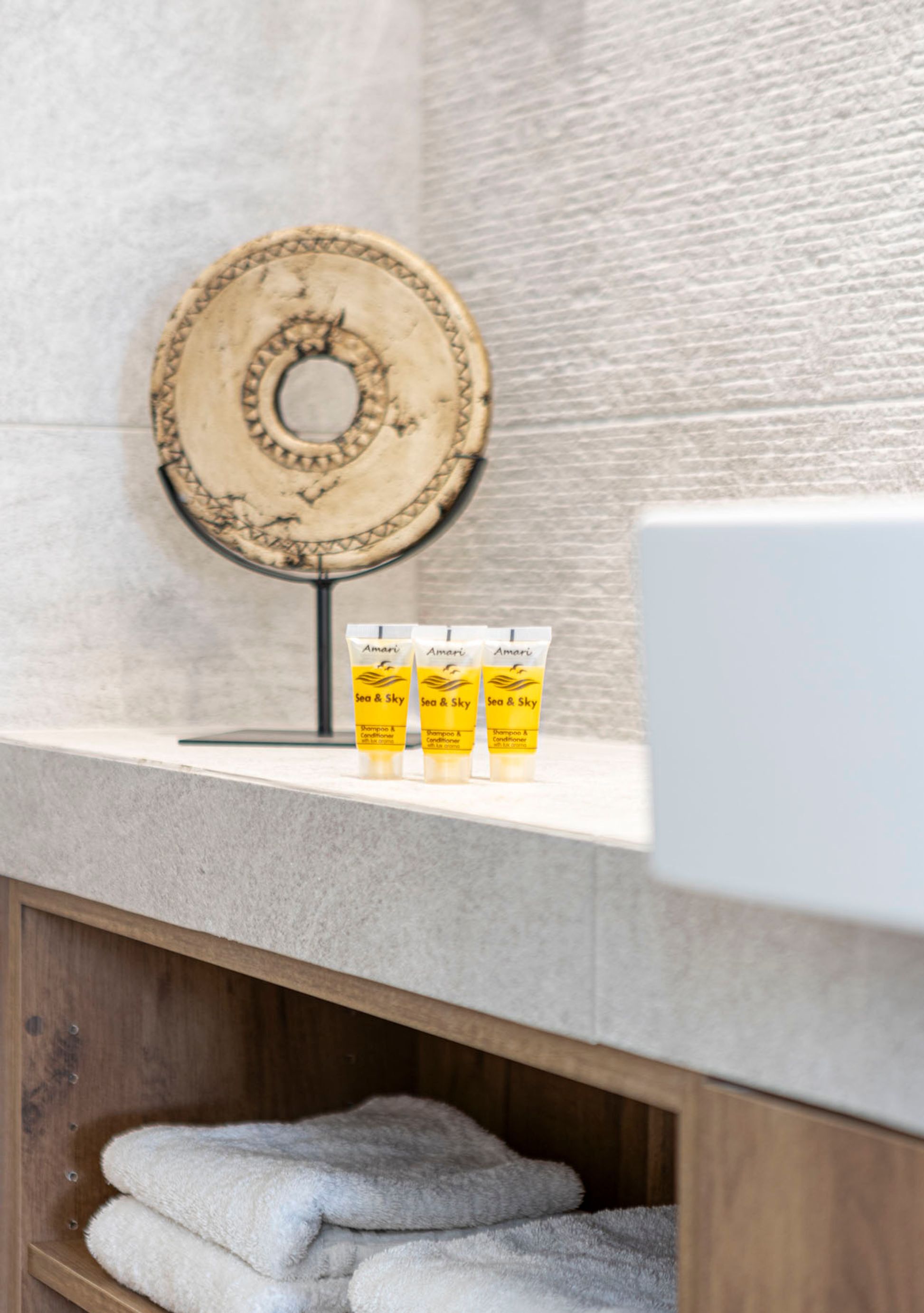 Une salle de bain avec une étagère en bois sur laquelle sont posées trois bouteilles de shampoing et un miroir rond accroché au mur.