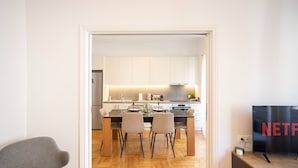 A modern kitchen with white cabinets, a dining table with chairs, and a TV displaying the Netflix logo. - Elegant 3-bedroom Retreat in the Heart of Kolonaki (Athens)