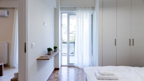 A bedroom with a bed, a wardrobe, a radiator, a shelf with a plant, and a view of the outside. - Modern 2-bedroom Apartment in Downtown Glyfada (Glyfada)
