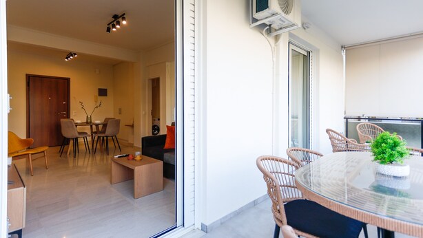 A modern living room with a glass dining table, wicker chairs, a sofa, and a coffee table. - Modern 2-bedroom Apartment in Downtown Glyfada (Glyfada)