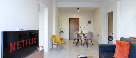 A modern living room with a flat-screen TV, a sofa, a coffee table, and a dining area with chairs and a table.