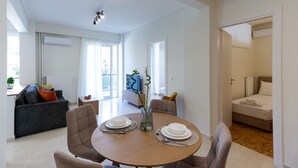 A modern living room with a dining table set for two, a sofa, and a TV in the background. - Modern 2-bedroom Apartment in Downtown Glyfada (Glyfada)