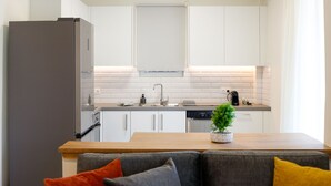 A modern kitchen with white cabinets, a built-in oven, and a dining area with a wooden table and a sofa. - Modern 2-bedroom Apartment in Downtown Glyfada (Glyfada)