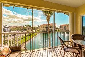 A balcony with a view of a body of water, a palm tree, and buildings in the background.