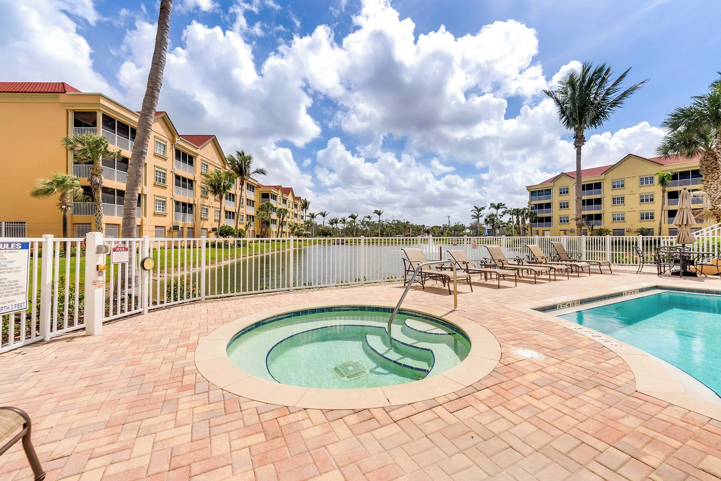 A pool area with a hot tub, lounge chairs, and a fenced pool.