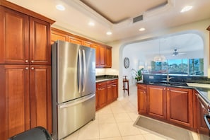 Una cocina con armarios de madera, un refrigerador de acero inoxidable, una encimera de granito y vistas a una zona de comedor a través de un arco.
