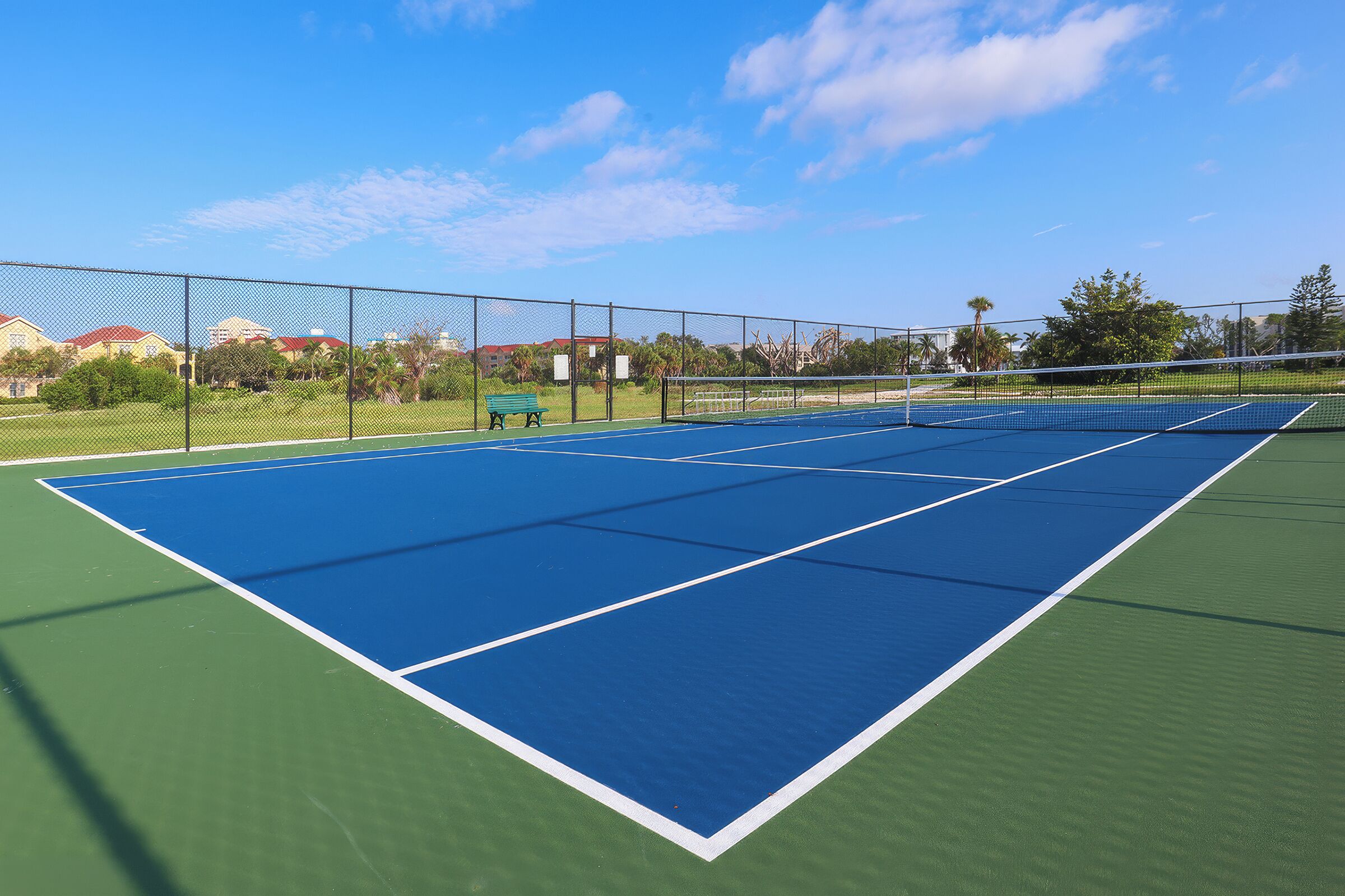 A tennis court with a net, surrounded by a chain-link fence, and a bench.
