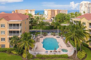 A resort with a central swimming pool, surrounded by palm trees and a view of the ocean.