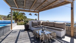 A covered outdoor seating area with a pool, a sofa, and a glass table.