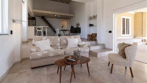 A spacious living area with a sofa, a coffee table, and a chair. A staircase leads to an upper level.