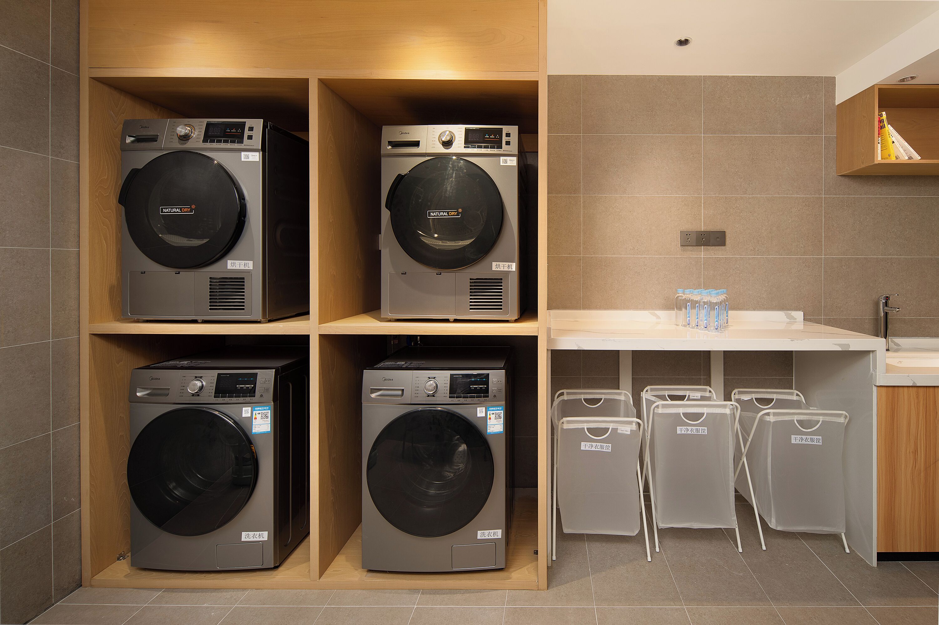 A laundry room with four washing machines, a sink, and four laundry baskets.