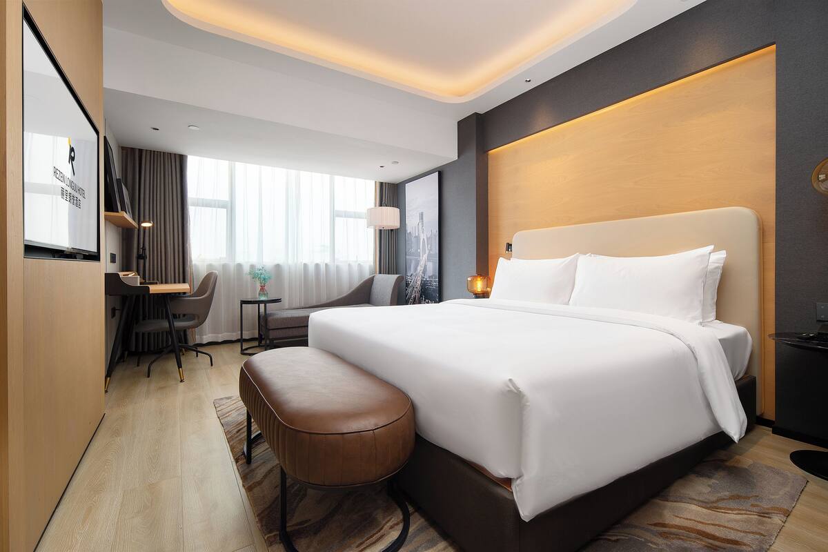 A modern hotel room with a large bed, a desk, and a comfortable seating area.