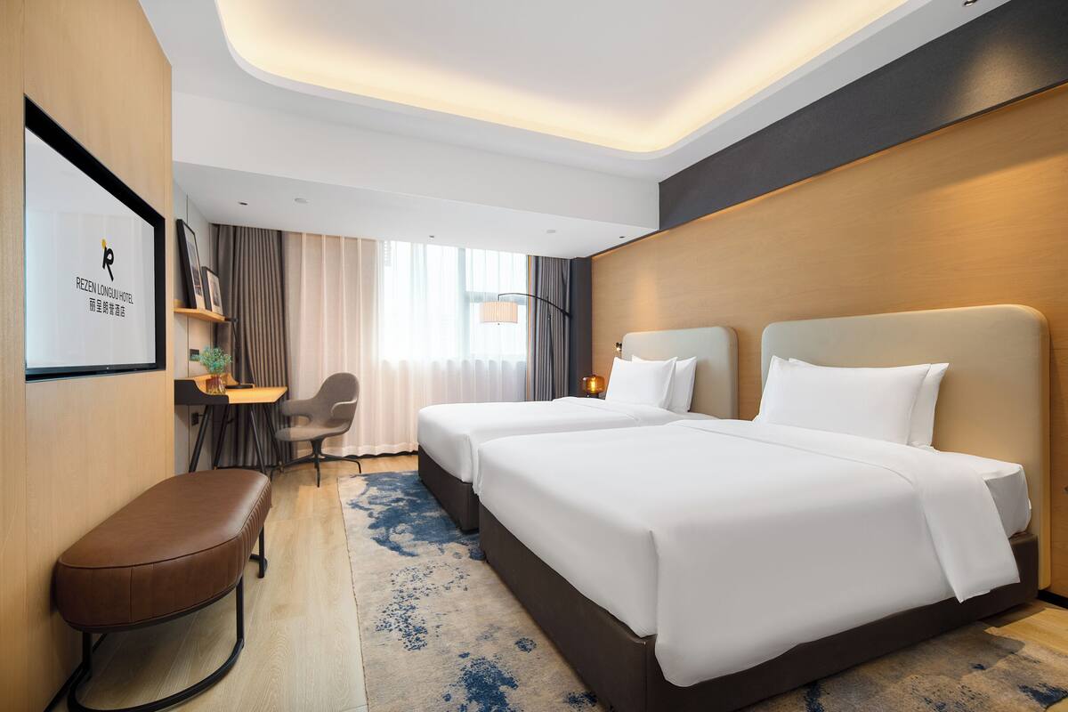 A hotel room with two beds, a desk, a chair, and a bench.