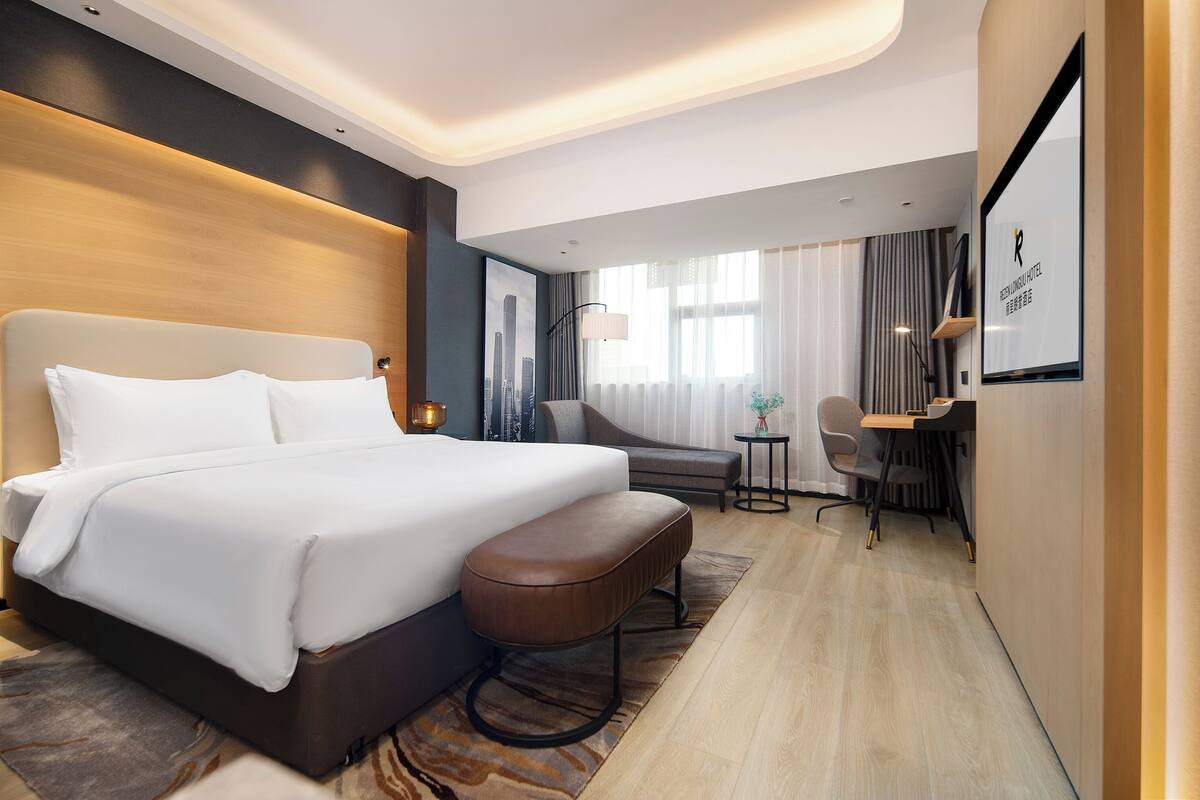 A modern hotel room with a large bed, a desk, and a chair.