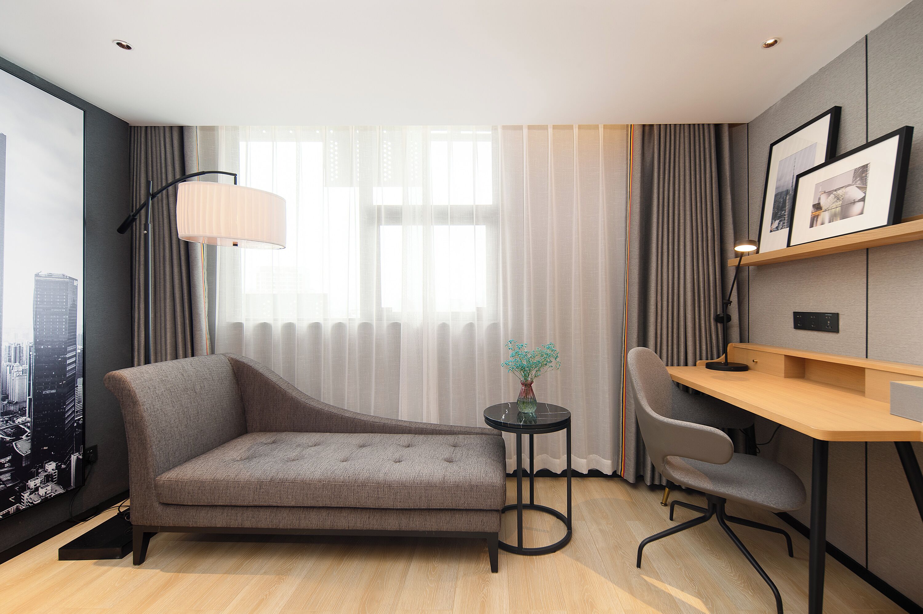 Una habitación de hotel moderna con sofá, escritorio, silla, lámpara y ventana con cortinas.