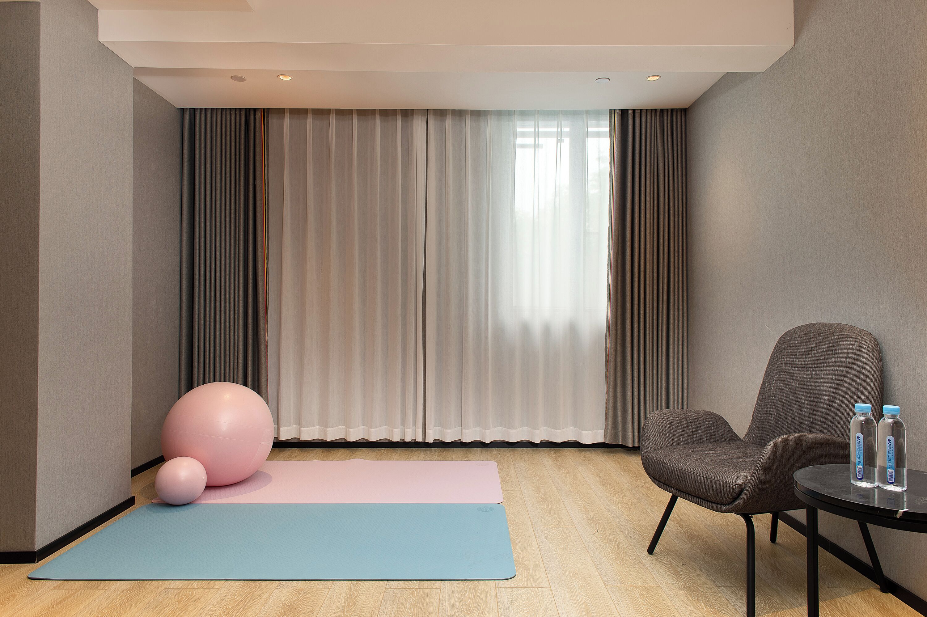 A room with a yoga mat, exercise ball, chair, and water bottles.