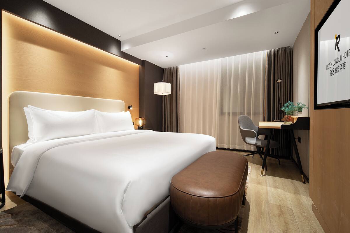 A hotel room with a large bed, a desk, and a chair.