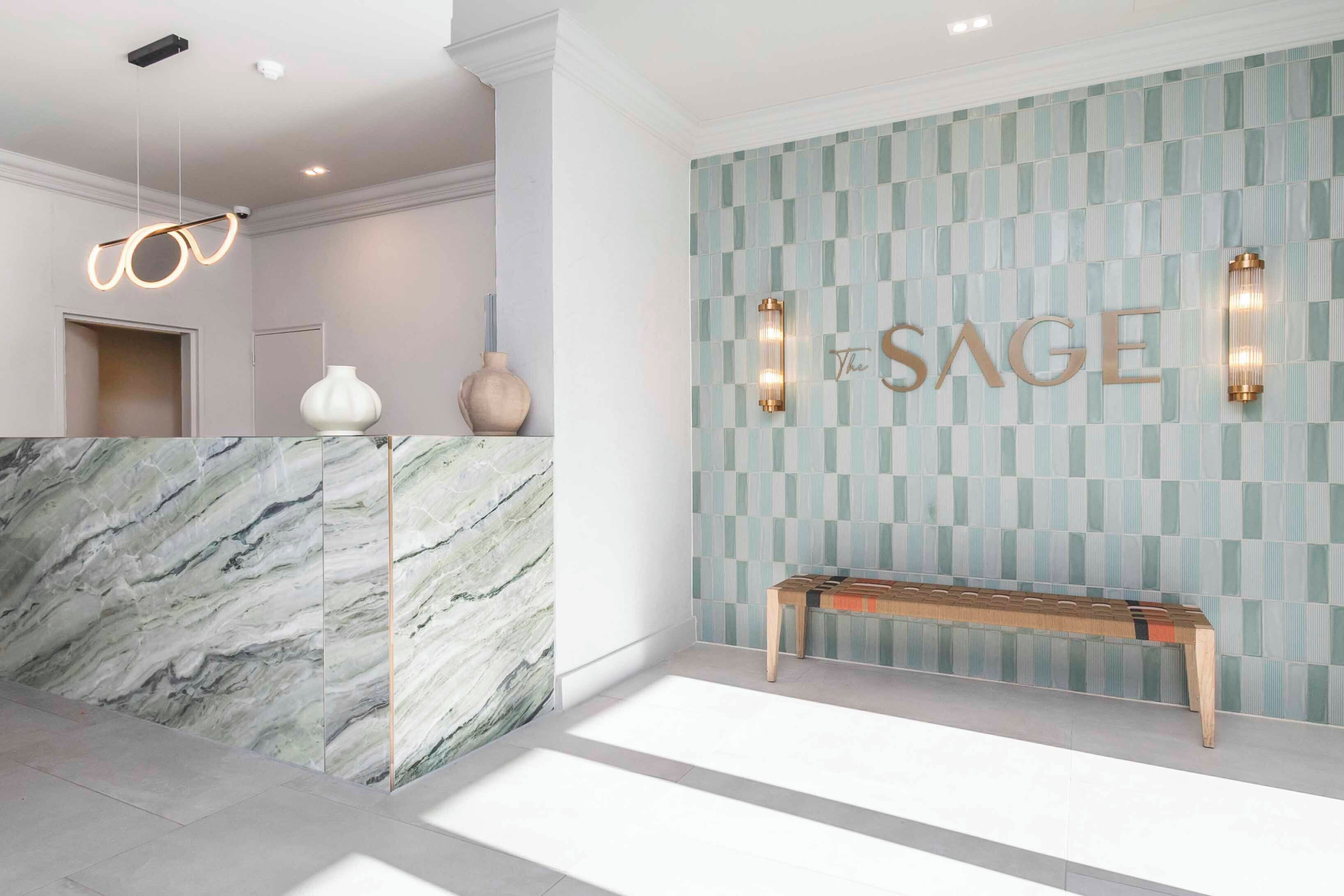 A reception area with a marble counter, a bench, and a wall with 'The SAGE' sign.