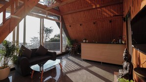 A modern interior with a wooden ceiling, a glass table, a sofa, a Buddha statue, and a kitchen area. - The Offroad Homestay (Dehradun)