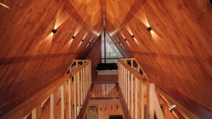 A wooden attic bedroom with a sloped ceiling, a central window, and a bed with a black headboard. - The Offroad Homestay (Dehradun)