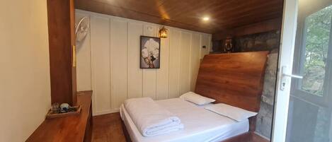 A bedroom with a wooden headboard, a bed with white linens, a wooden nightstand, a wall-mounted fan, and a framed picture.