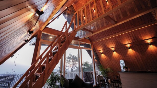 A spacious room with a high ceiling, wooden beams, and a large window offering a view of the outdoors. - The Offroad Homestay (Dehradun)