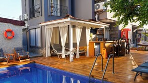 An indoor swimming pool with a wooden deck, lounge chairs, and a bar area. - Kekik Alaçatı Otel (Cesme)