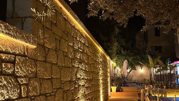 A stone wall with warm lighting, a wooden pathway, and outdoor seating areas. - Kekik Alaçatı Otel (Cesme)
