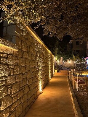 A stone wall with warm lighting, a wooden pathway, and outdoor seating areas. - Kekik Alaçatı Otel (Cesme)