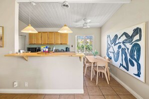 A kitchen with wooden cabinets, a central island, pendant lights, a ceiling fan, and a large abstract painting.