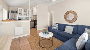 Un salon avec un canapé bleu, une table basse ronde et une cuisine en arrière-plan.